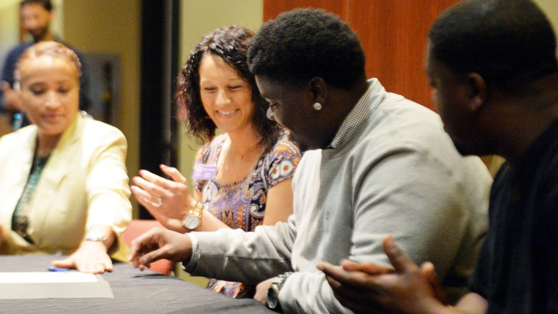 Walter signs paperwork to attend Young Harris College as admissions coordinator Kayla Walker (left) and his uncle Charles look on during a Project Grad ceremony at the Atlanta Public Schools headquarters in May. Kent D. Johnson/AJC